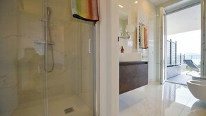 Un baño moderno con ducha envuelta en vidrio, un espejo grande y vistas al exterior.