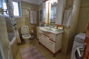 Un baño con inodoro, lavabo, espejo y lavadora.