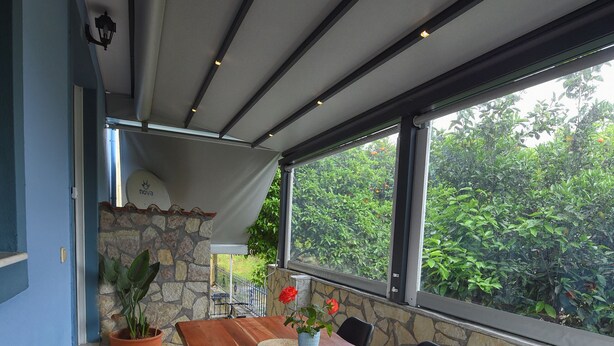 Un espace repas moderne avec une table et des bancs en bois, un mur en pierre et de grandes fenêtres donnant sur un paysage verdoyant.