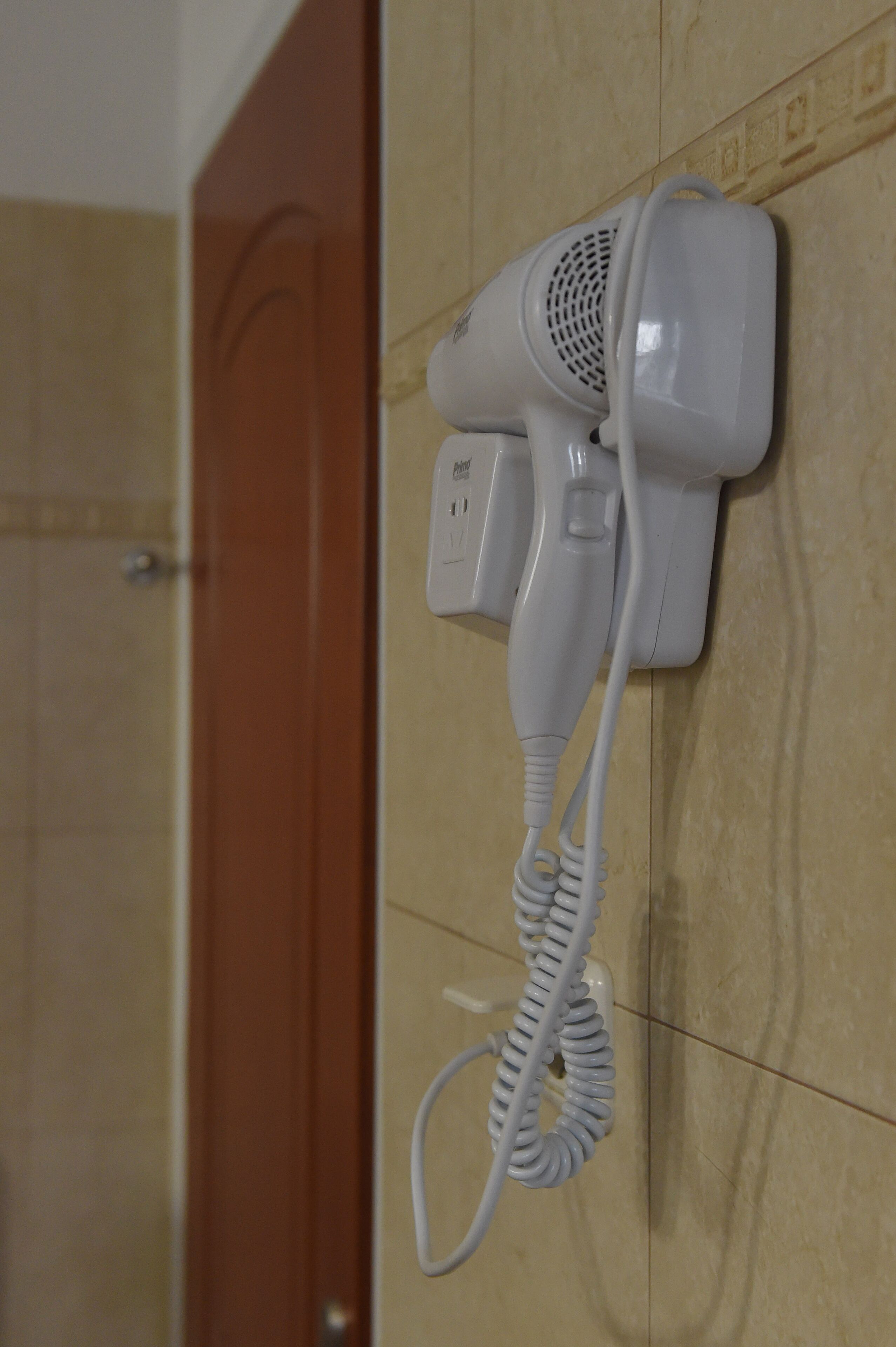 Un asciugacapelli fissato a una parete rivestita di piastrelle in un bagno.