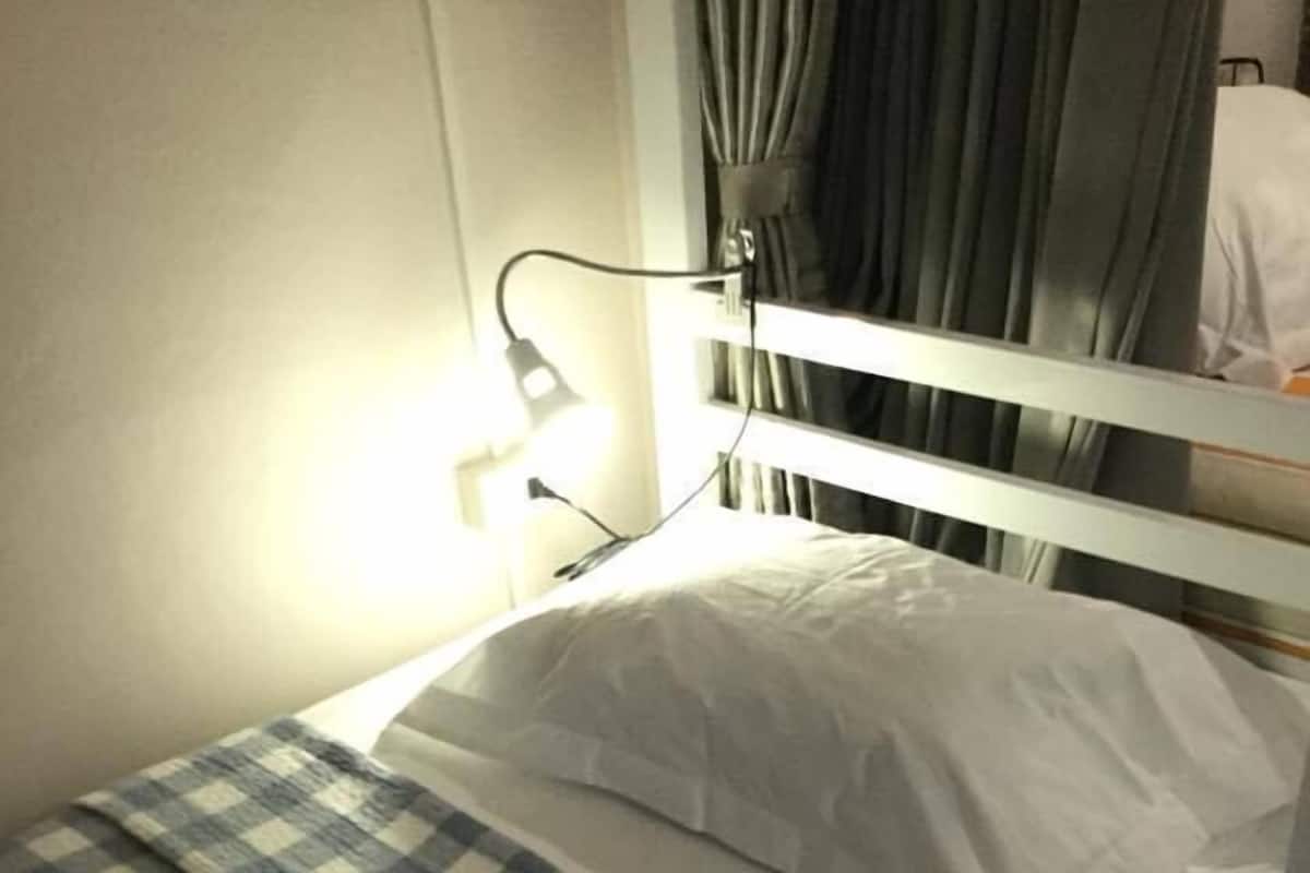 A single bed with a checkered blanket, white pillows, and a bedside lamp.