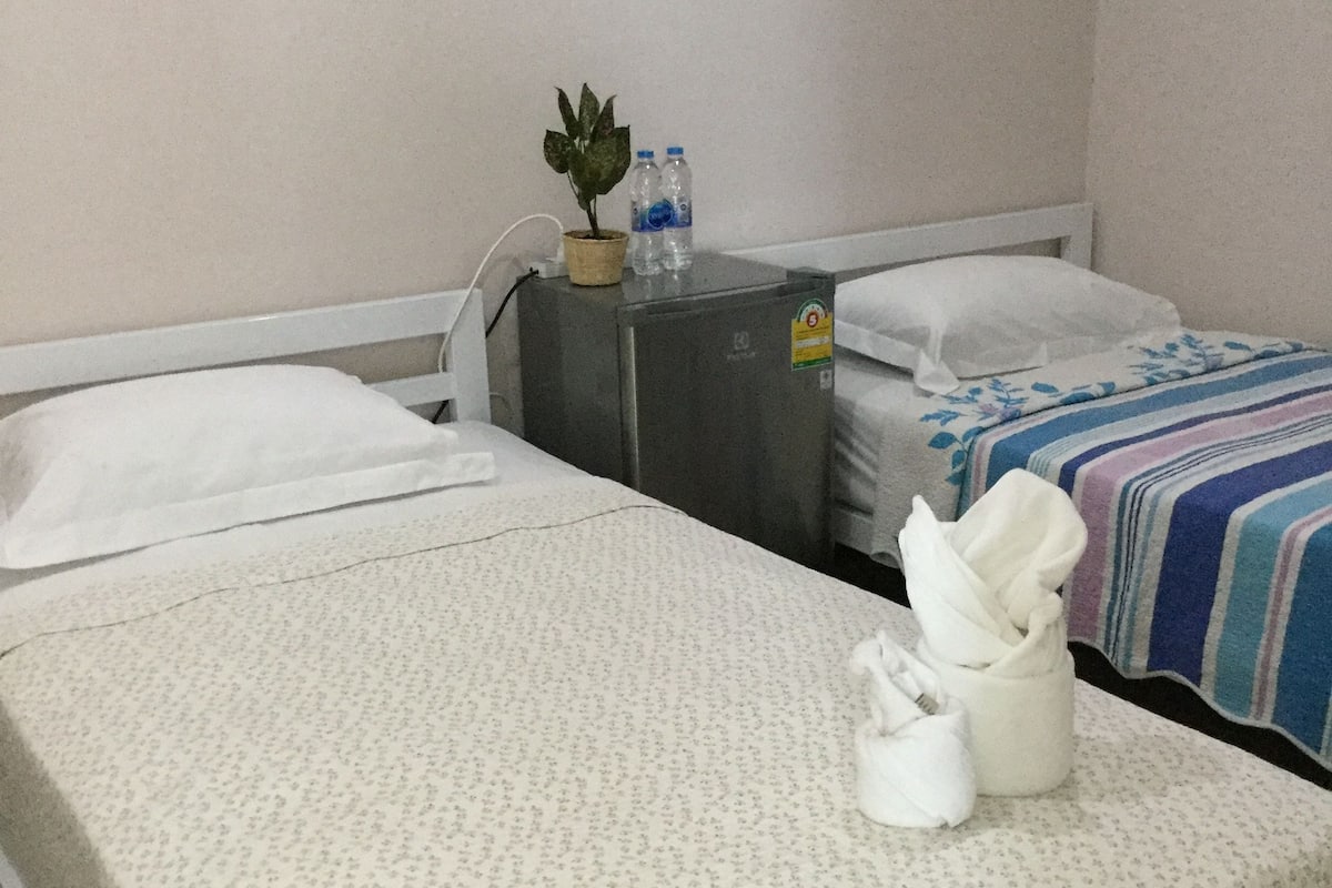 A hotel room with two beds, a small refrigerator, a potted plant, and a bottle of water.