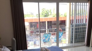 A hotel room with a large bed, a flat-screen TV mounted on the wall, and a view of a swimming pool and building through the window. - Chogun Hostel (Chumphon)