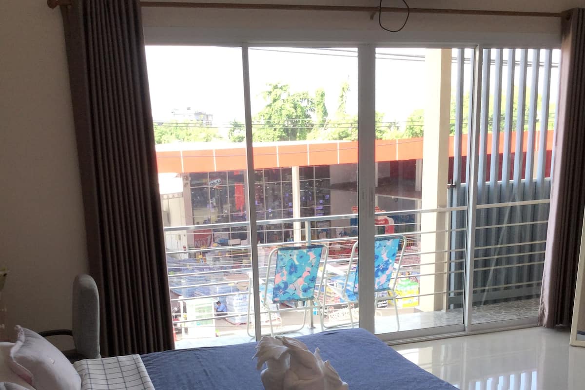 A hotel room with a large bed, a flat-screen TV mounted on the wall, and a view of a swimming pool and building through the window.