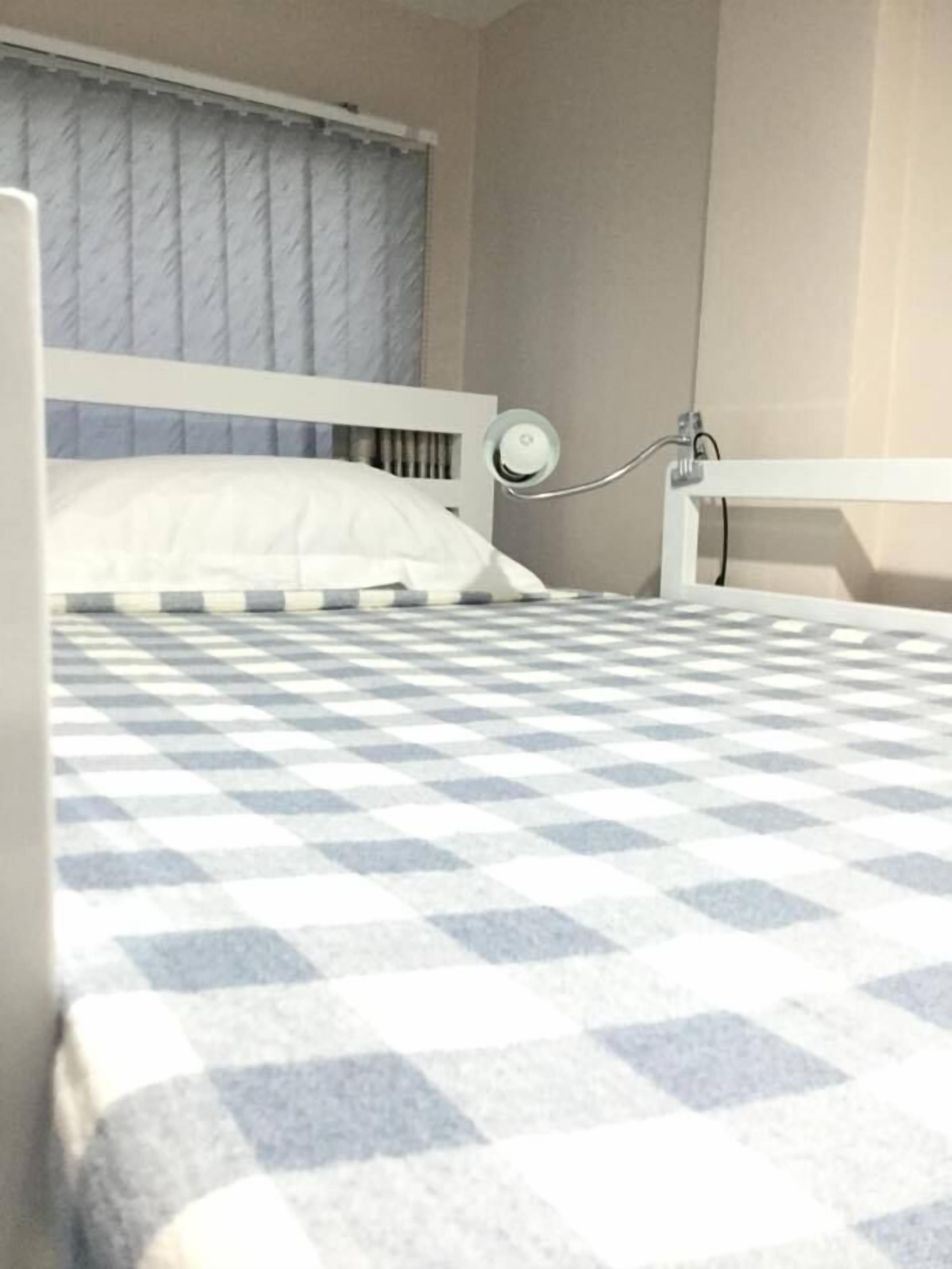 A bed with a checkered bedspread, a white headboard, and a bedside table with a lamp.