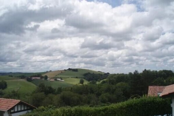 A rural landscape with rolling hills, a traditional building with a tiled roof, and a partly cloudy sky. - Apartment Pays Basque (Pyrénées-Atlantiques)