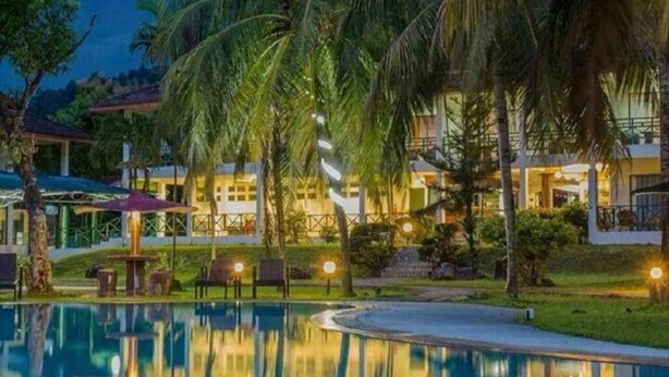 Een resort met een zwembad, palmbomen en verlichte gebouwen 's nachts.
