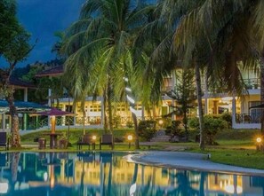 A resort with a swimming pool, palm trees, and well-lit buildings at night.