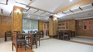 A spacious dining area with multiple wooden tables and chairs, a tiled floor, and brick-patterned walls. - TG Tashkent Hotel (New Delhi)