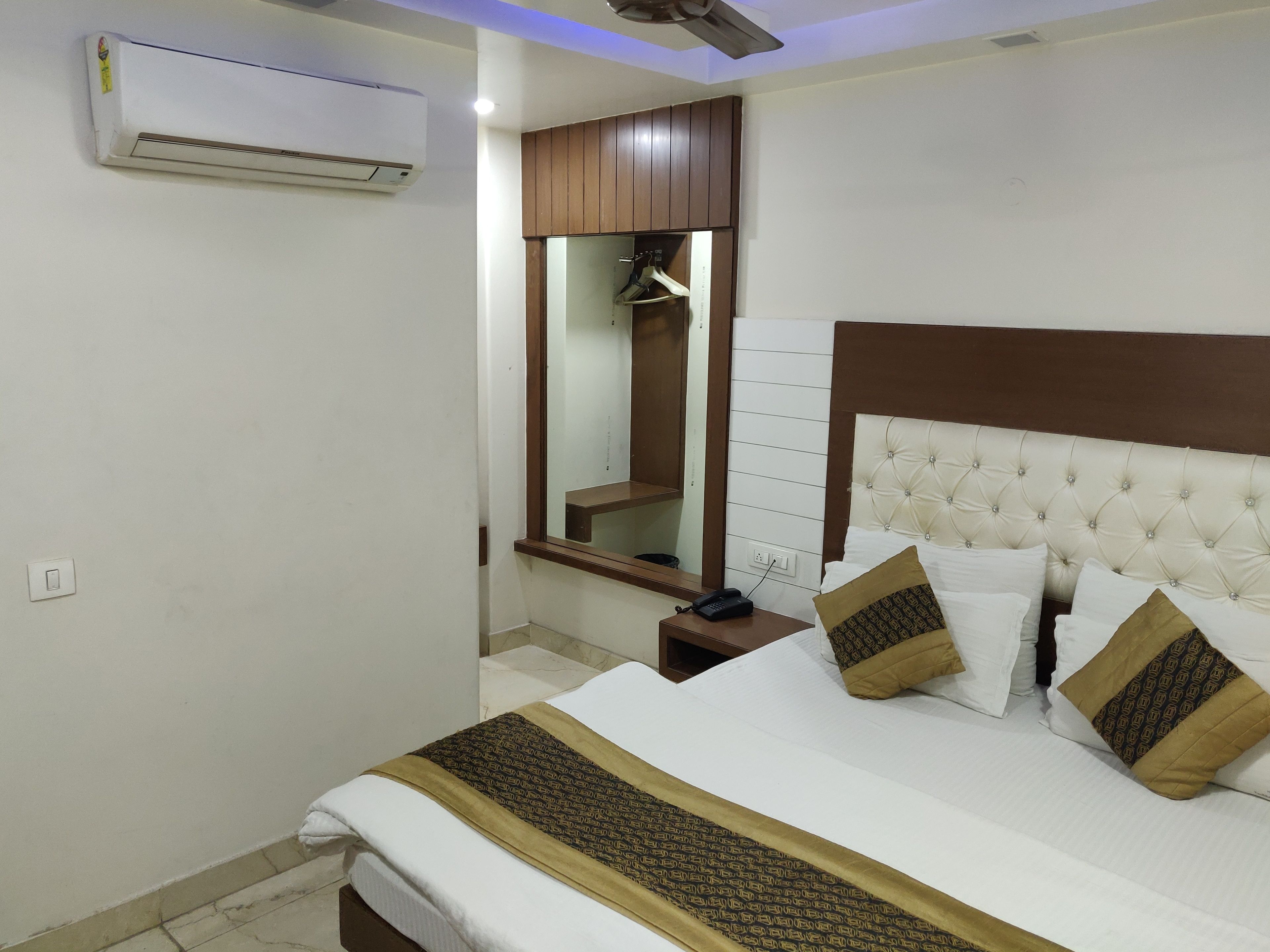A hotel room with a bed, a bedside table, a mirror, and an air conditioning unit.
