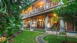 A two-story building with a covered porch, a garden with a curved pathway, and a staircase leading to the upper level. - Adi Jaya Cottages Jungle Suites by EPS (Ubud)