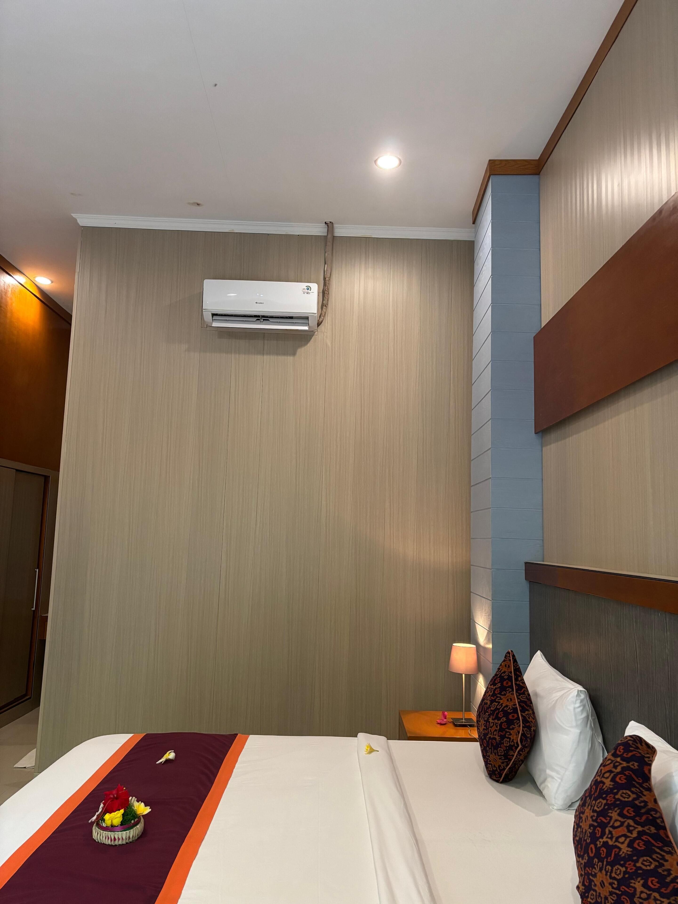 A hotel room with a bed, a nightstand, a lamp, and an air conditioning unit on the wall.