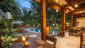 A wooden outdoor dining area with a pool and lush greenery in the background. - Adi Jaya Cottages Jungle Suites by EPS (Ubud)