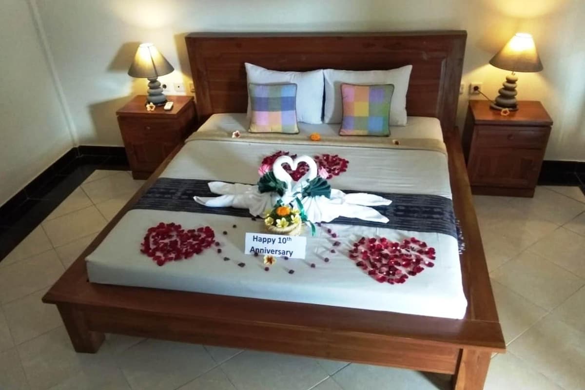 Uma cama bem arrumada com uma placa de 'Feliz 10º Aniversário', arranjos florais em formato de coração e uma decoração de cisne.