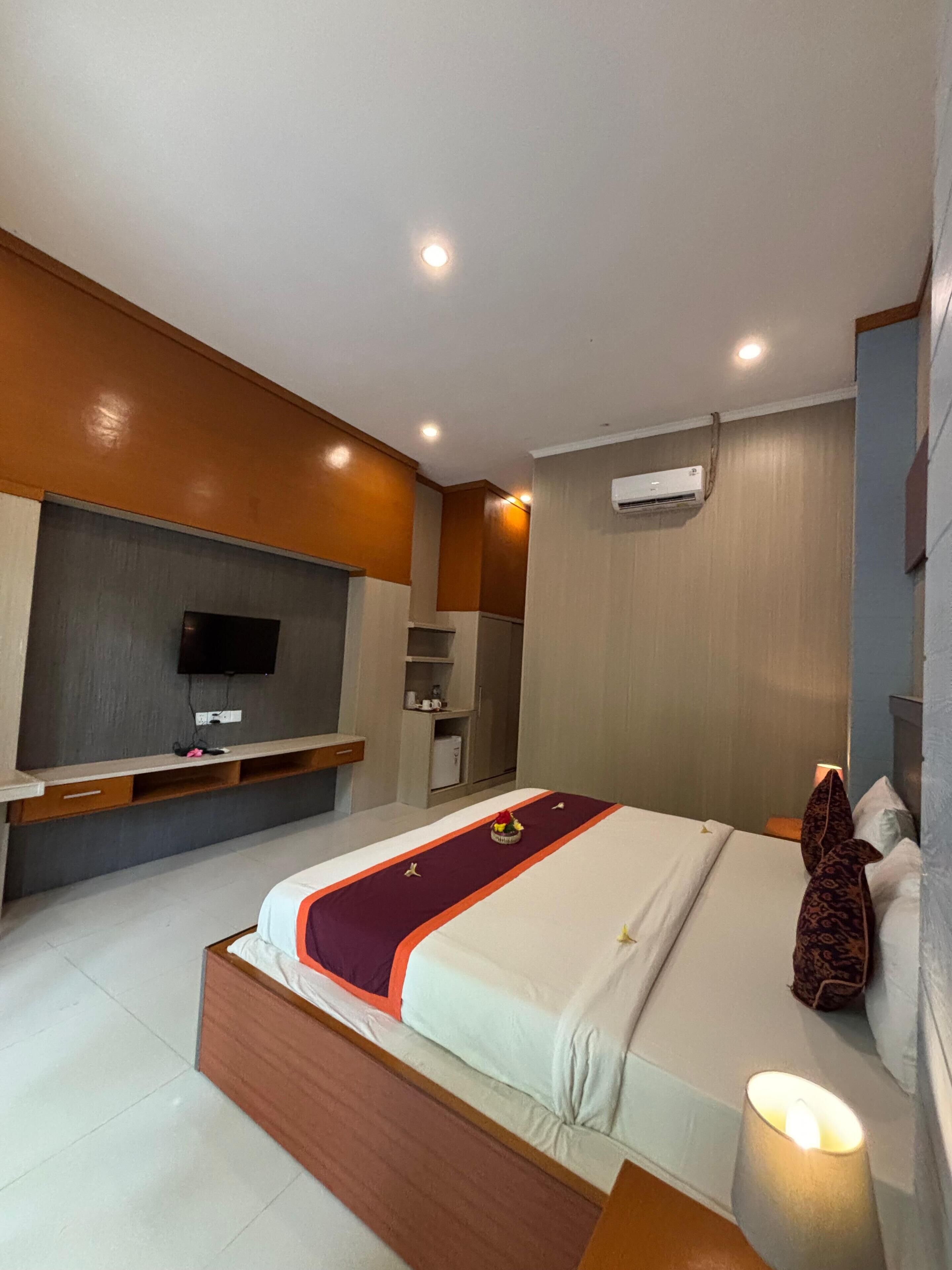 A hotel room with a bed, a TV, a wardrobe, and an air conditioning unit.