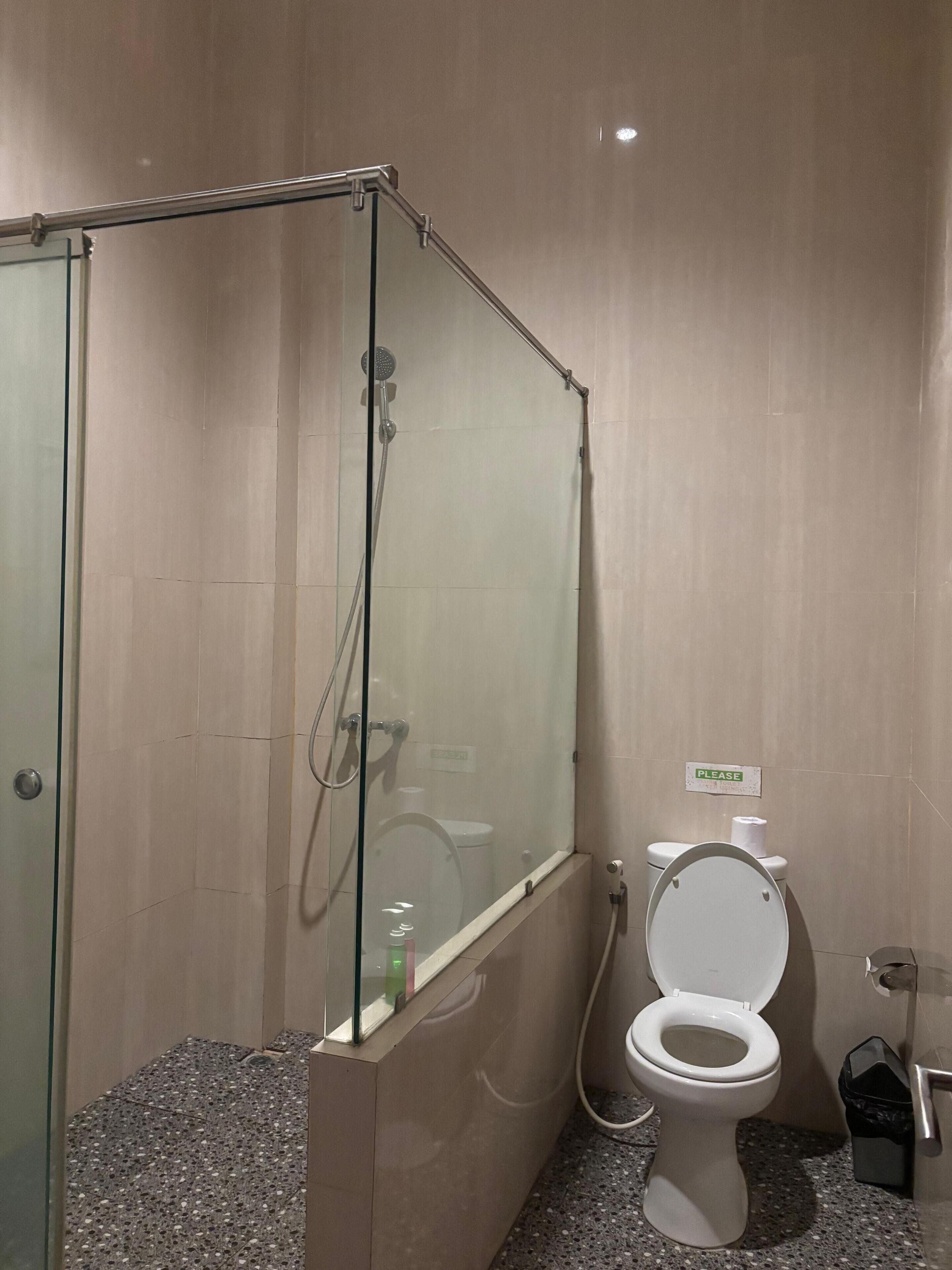 A bathroom with a glass-enclosed shower, a toilet, and a trash bin.