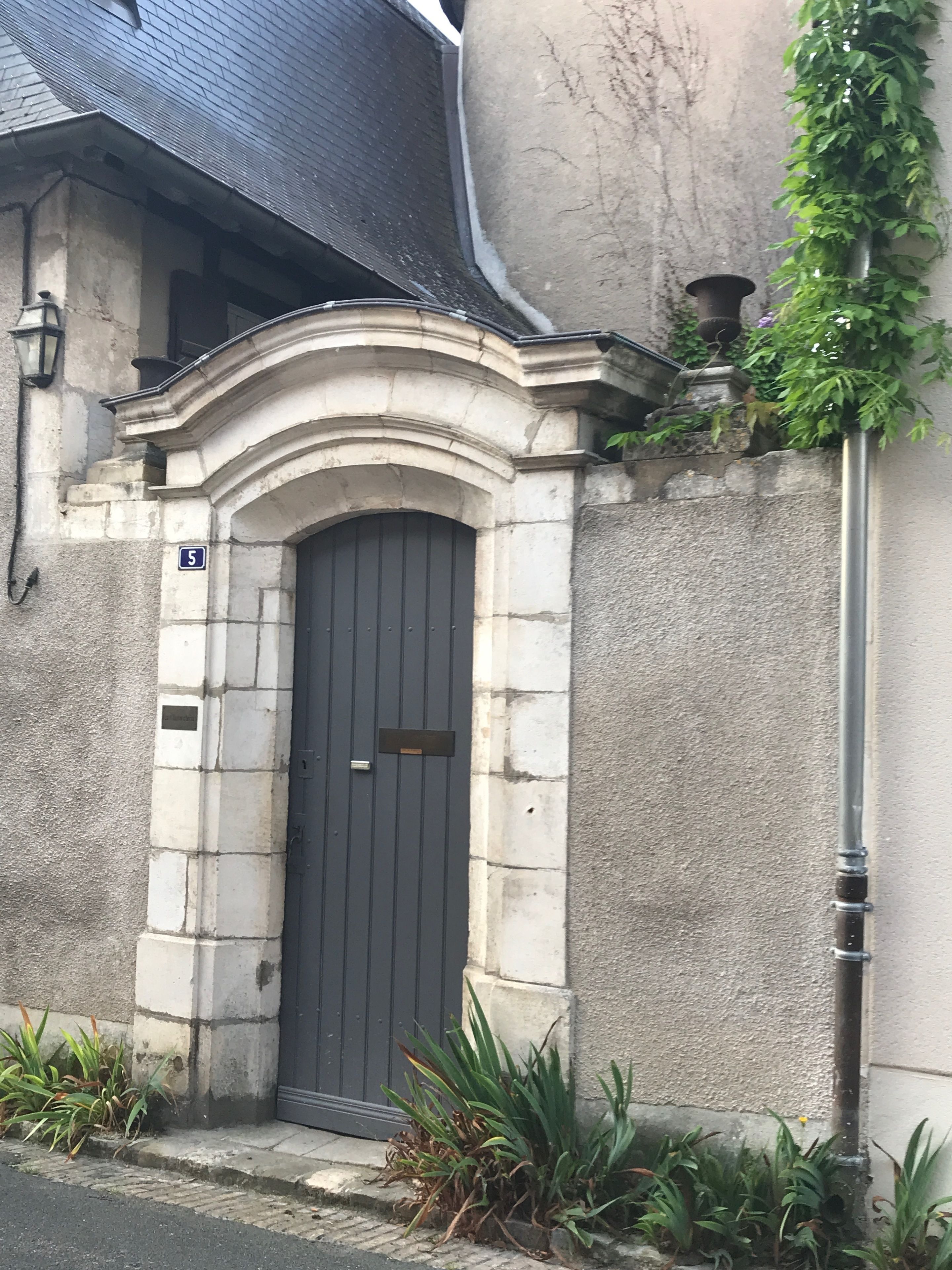 A stone building with a dark door, a small window, and a number '5' sign.