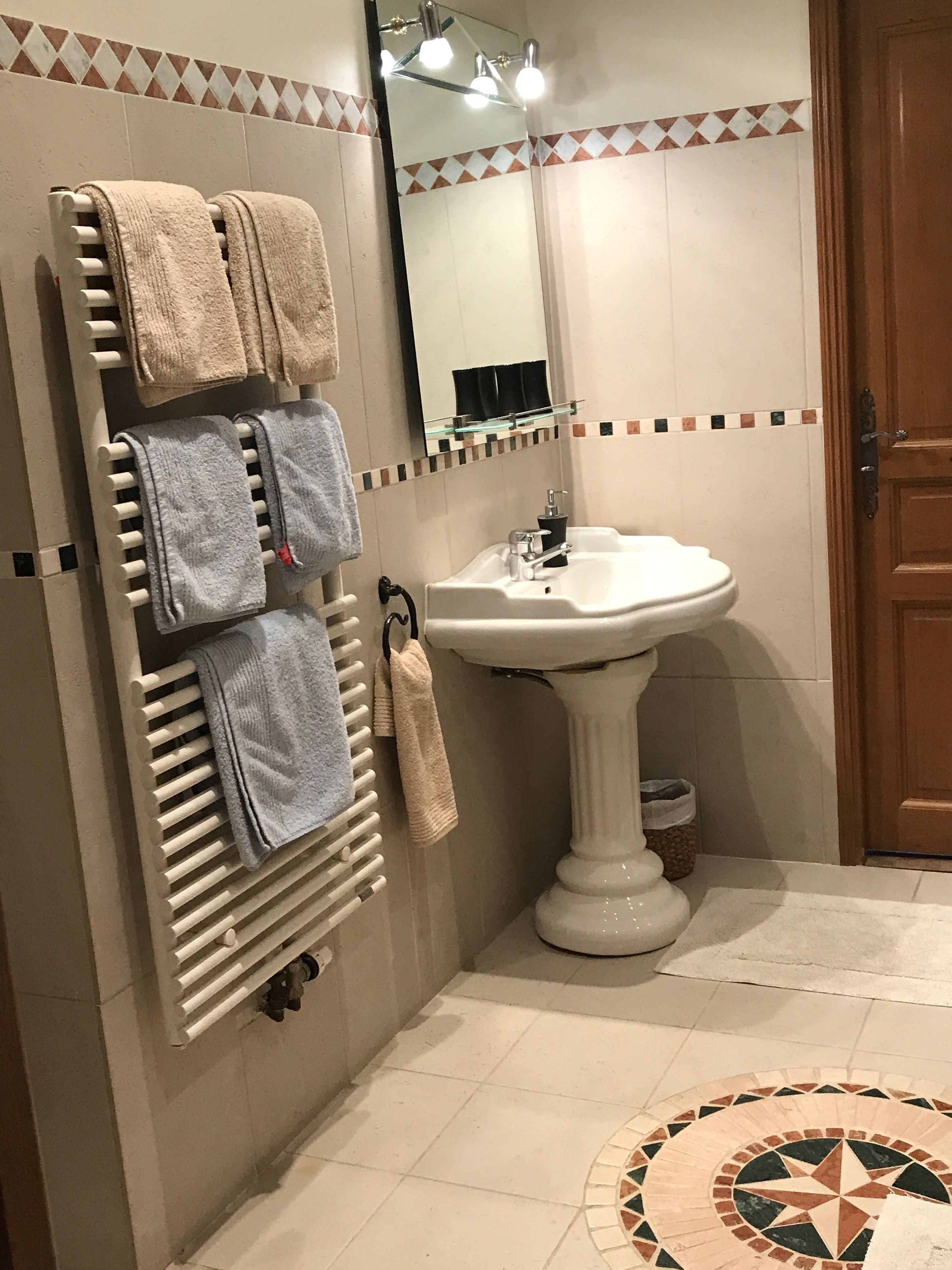 Un baño con un toallero que sostiene varias toallas, un lavamanos pedestal y un espejo encima.