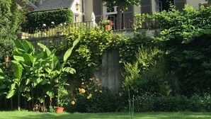 Un edificio tradicional con una torre cónica, un balcón y un jardín con plantas y flores en macetas.