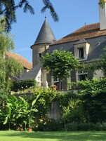 Un edificio tradicional con una torre cónica, un balcón y un jardín con plantas y flores en macetas.