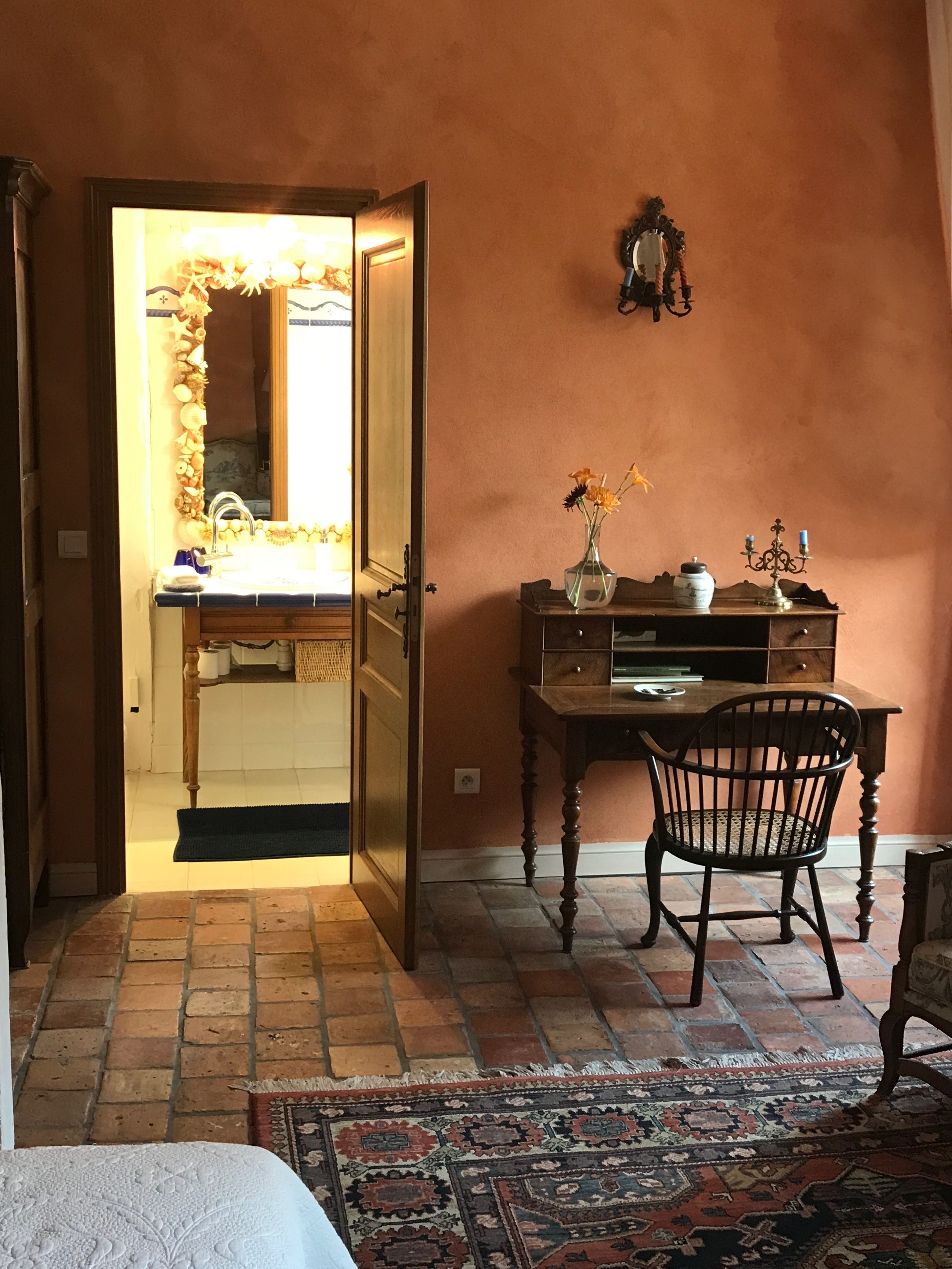 A room with a wooden desk, a chair, a mirror, and a rug.