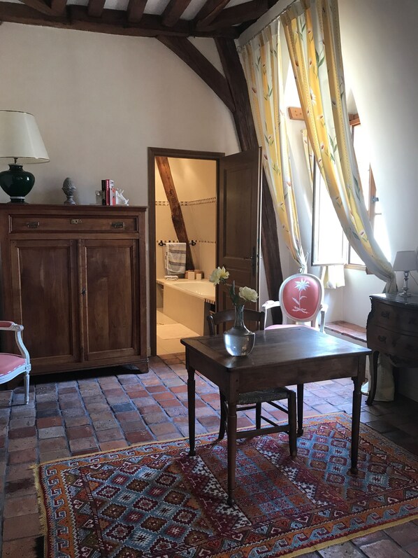 Una habitación acogedora con un armario de madera, una mesa con un florero, una alfombra estampada y una silla.