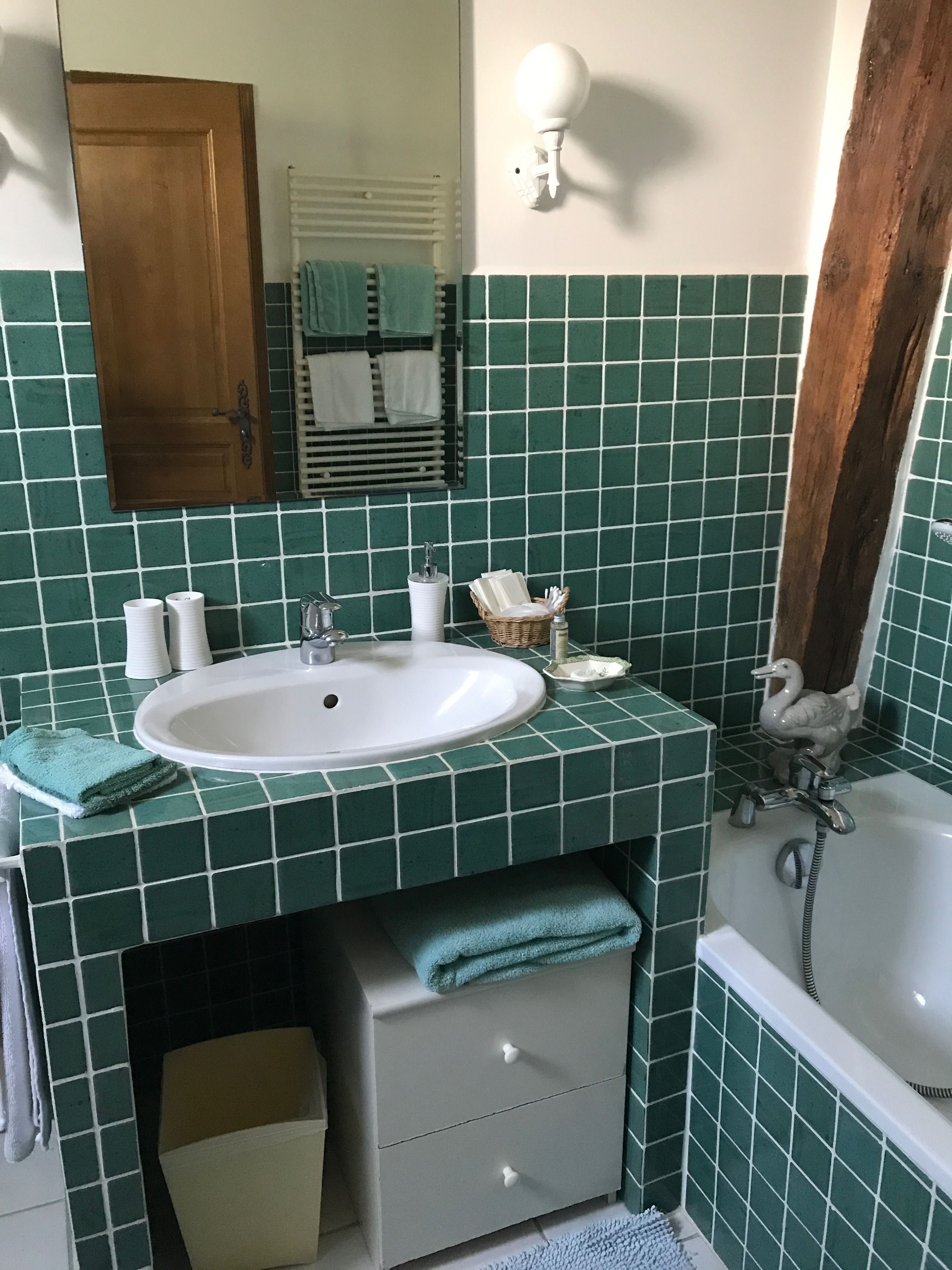 Un baño con un lavamanos blanco, azulejos verdes, una puerta de madera, un espejo y una zona de ducha.