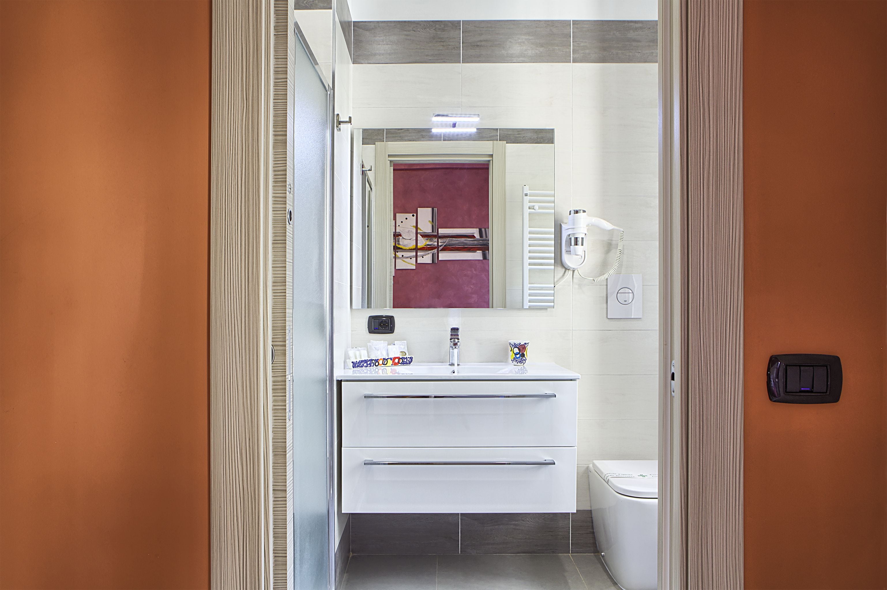 Ein modernes Badezimmer mit einem weißen Waschtisch, einem Spiegel, einem Handtuchhalter und einer Toilette.