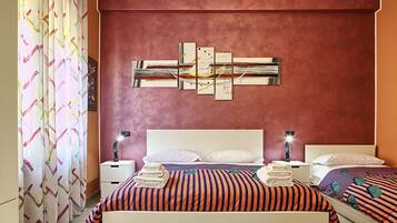 Quarto de hotel com uma cama grande, duas mesas de cabeceira com luminárias, uma obra de arte na parede e uma cortina estampada.