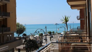 Un balcon avec vue sur la mer, un restaurant avec une terrasse, et un bâtiment sur lequel on peut lire l’inscription « Assicurazioni ».