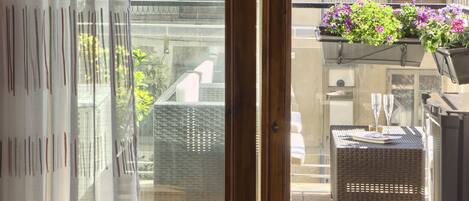 A balcony with wicker furniture, a hanging planter with flowers, and a glass door leading to the interior.