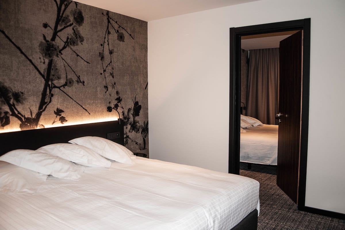 A hotel room with a large bed, a headboard with a floral design, and a door leading to another room.