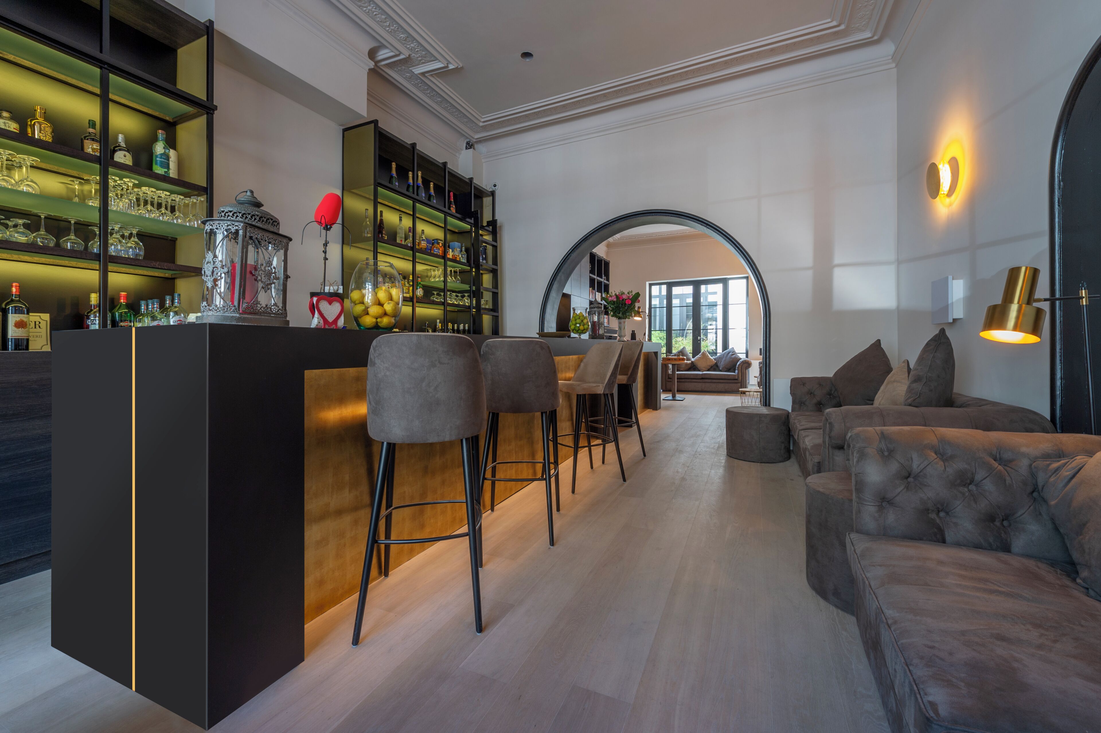 A modern bar area with a wooden counter, bar stools, and a variety of bottles and glasses.