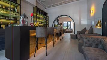 A modern bar area with a wooden counter, bar stools, and a variety of bottles and glasses.