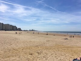 A wide sandy beach with people walking and relaxing.