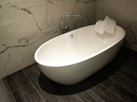 A modern bathroom with a freestanding bathtub, marble walls, and dark wooden flooring.