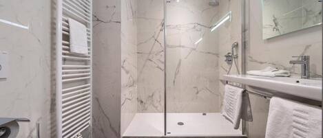 Un baño moderno con ducha envuelta en vidrio, lavamanos blanco y espejo grande.