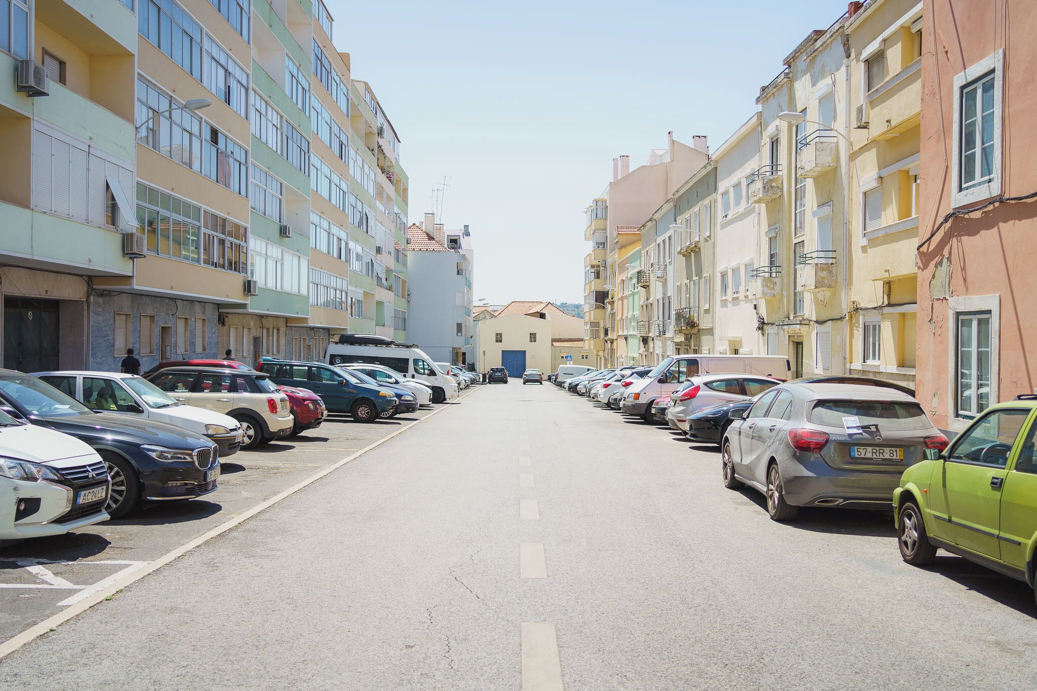 Fila di auto parcheggiate lungo una strada fiancheggiata da edifici a più piani.