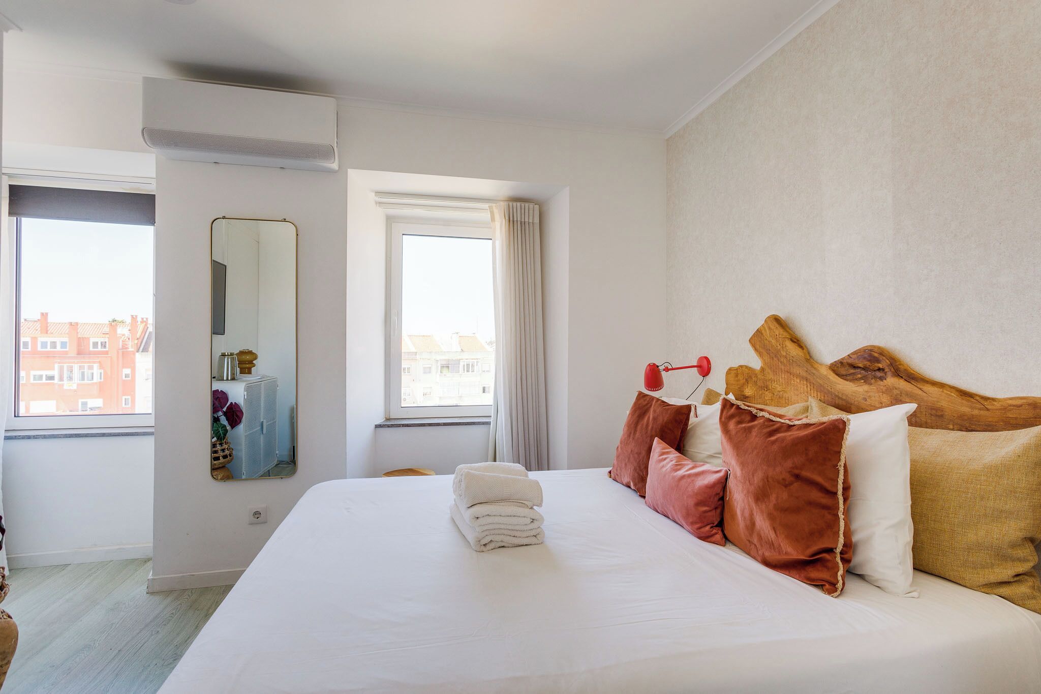 Habitación de hotel con una cama grande, un espejo, una ventana con cortinas y vistas a edificios.