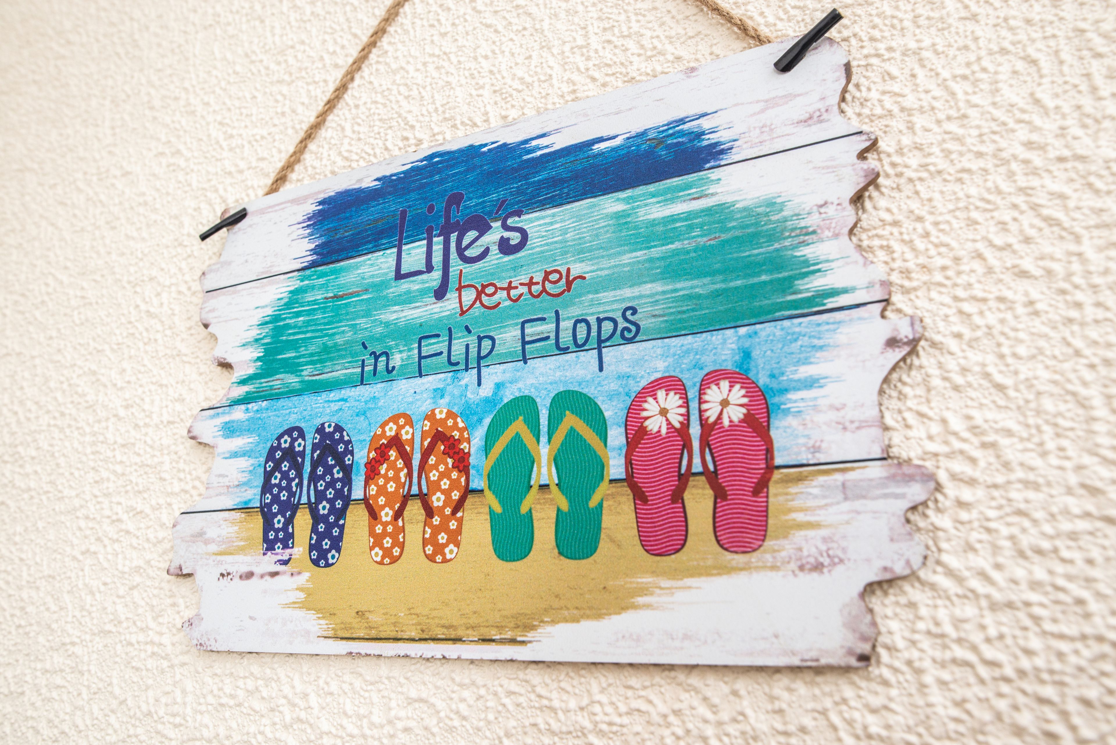 A wooden sign with flip flops and the text "Life's better in Flip Flops" on a textured wall.