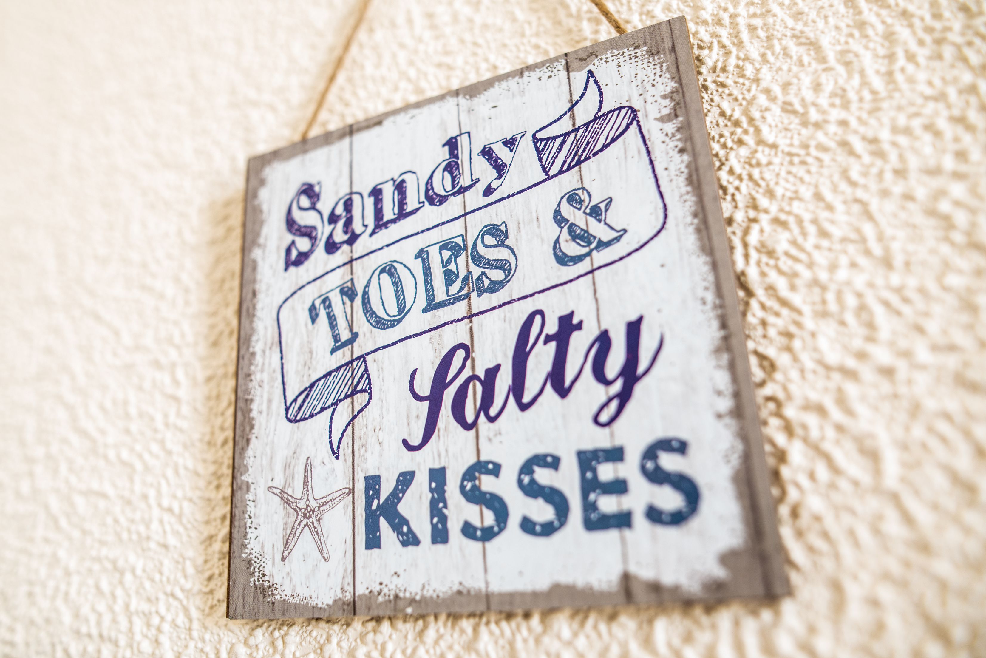A sign with the text "Sandy toes & salty kisses" on a textured surface.