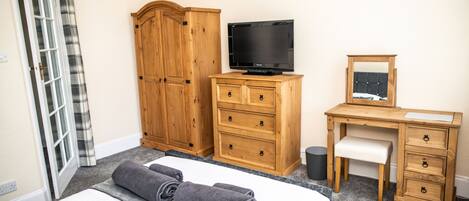 A hotel room with a bed, a wooden wardrobe, a desk with a chair, a television, and a mirror.