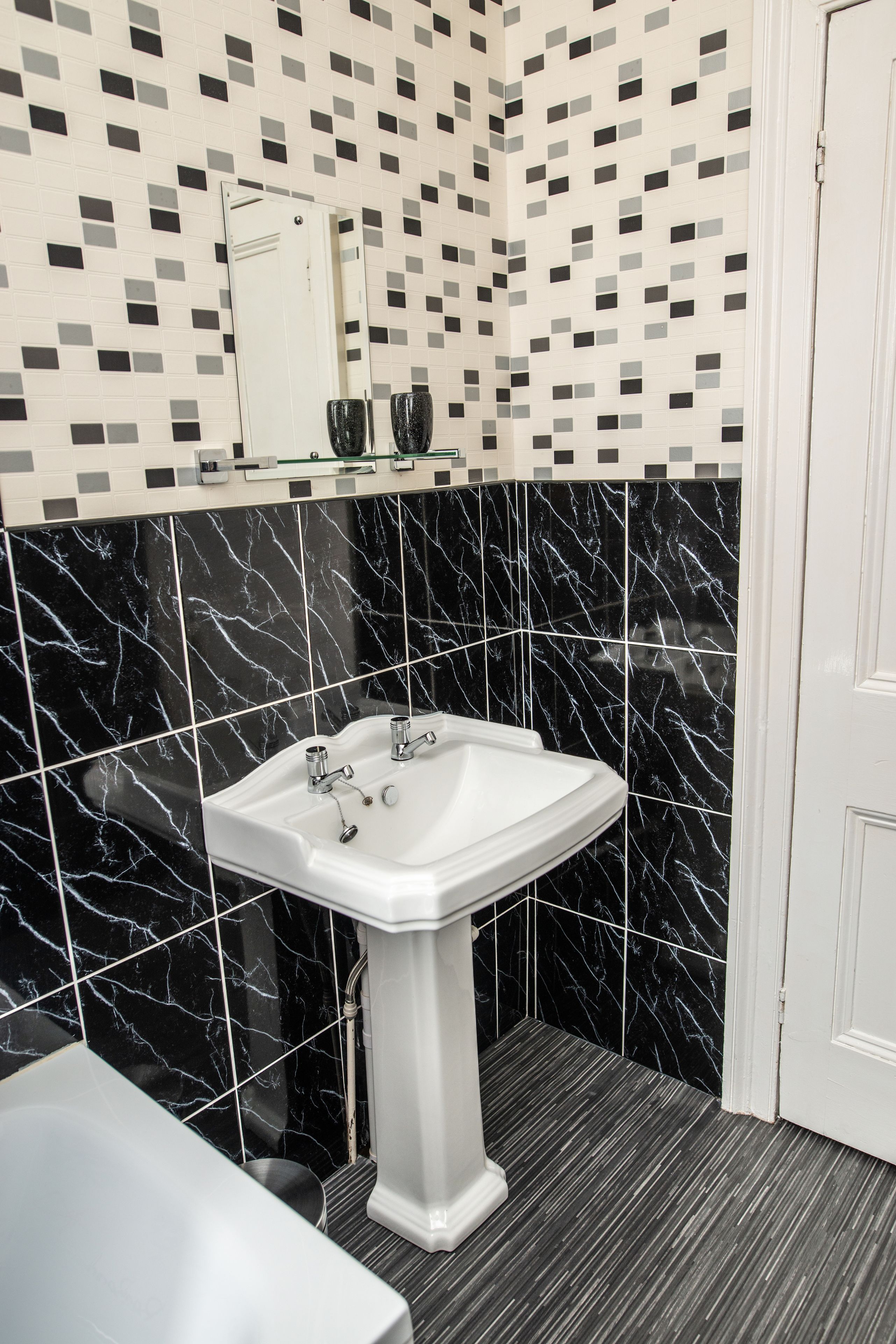 A bathroom with a white pedestal sink, black marble tiles, and a tiled backsplash with a geometric pattern.