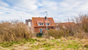 A two-story brick house with a red-tiled roof, surrounded by overgrown vegetation. - Sable d'O (Ostend)