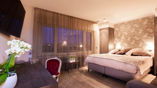 A hotel room with a bed, a desk with a chair, a TV, and a window with curtains. - Sable d'O (Ostend)