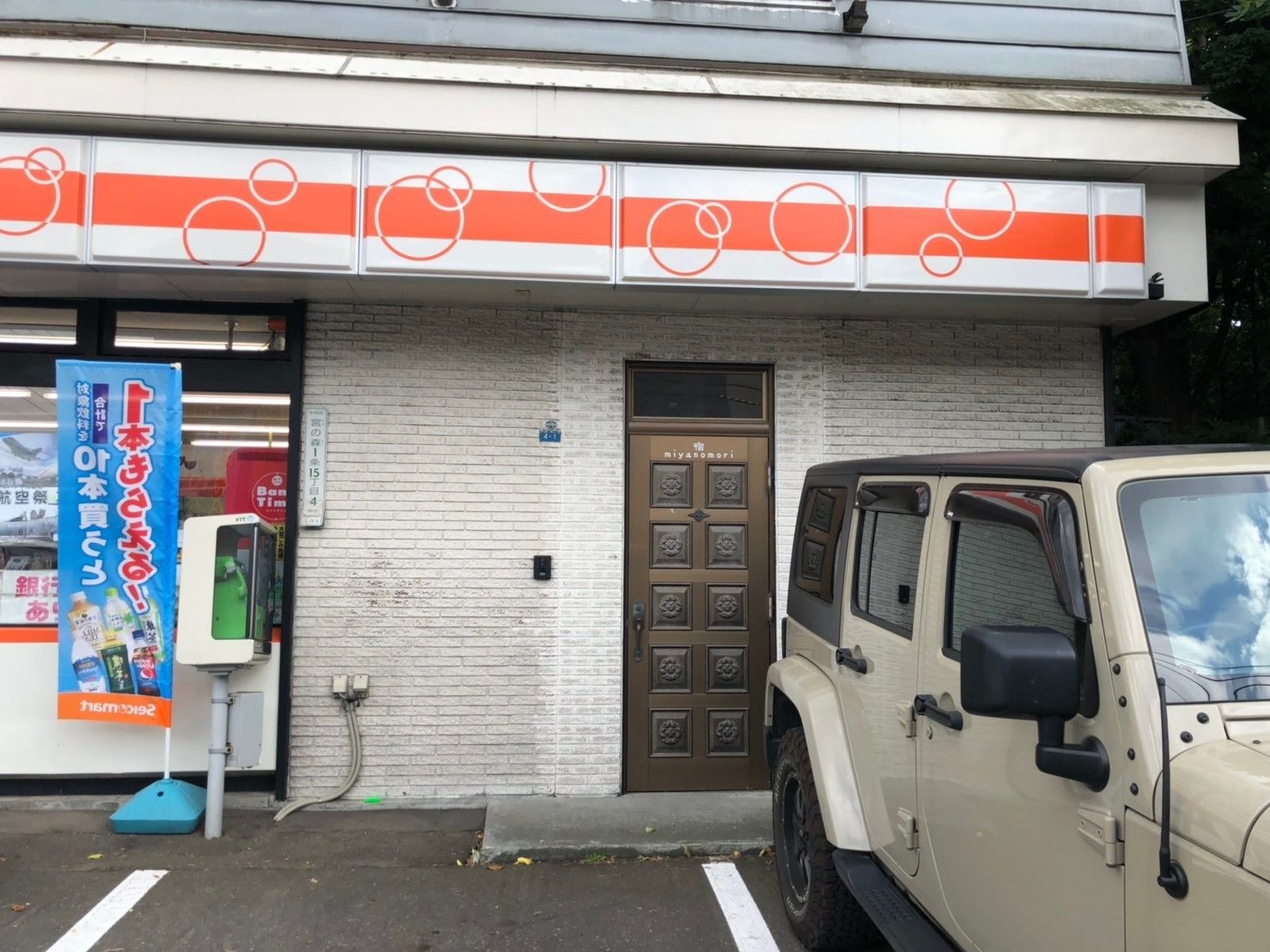 A building with a white and orange facade, a brown door with a grid pattern, and a parked off-road vehicle.
