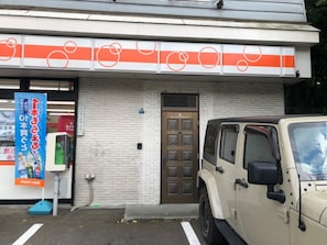 Un edificio con fachada blanca y naranja, una puerta marrón con diseño de cuadrícula, y un vehículo todoterreno estacionado.