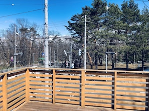 Una terraza de madera con barandilla de metal, rodeada de árboles y postes de electricidad.