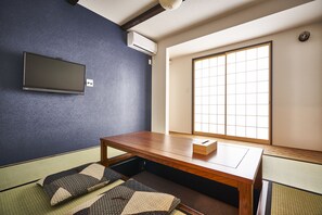 A tatami mat room with a low wooden table, a television mounted on the wall, and a shoji screen window. - Tomari-gi (Kyoto)