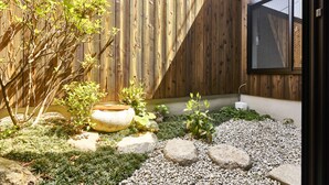Een tuin met een houten hek, een stenen plantenbak en een raam met hor.